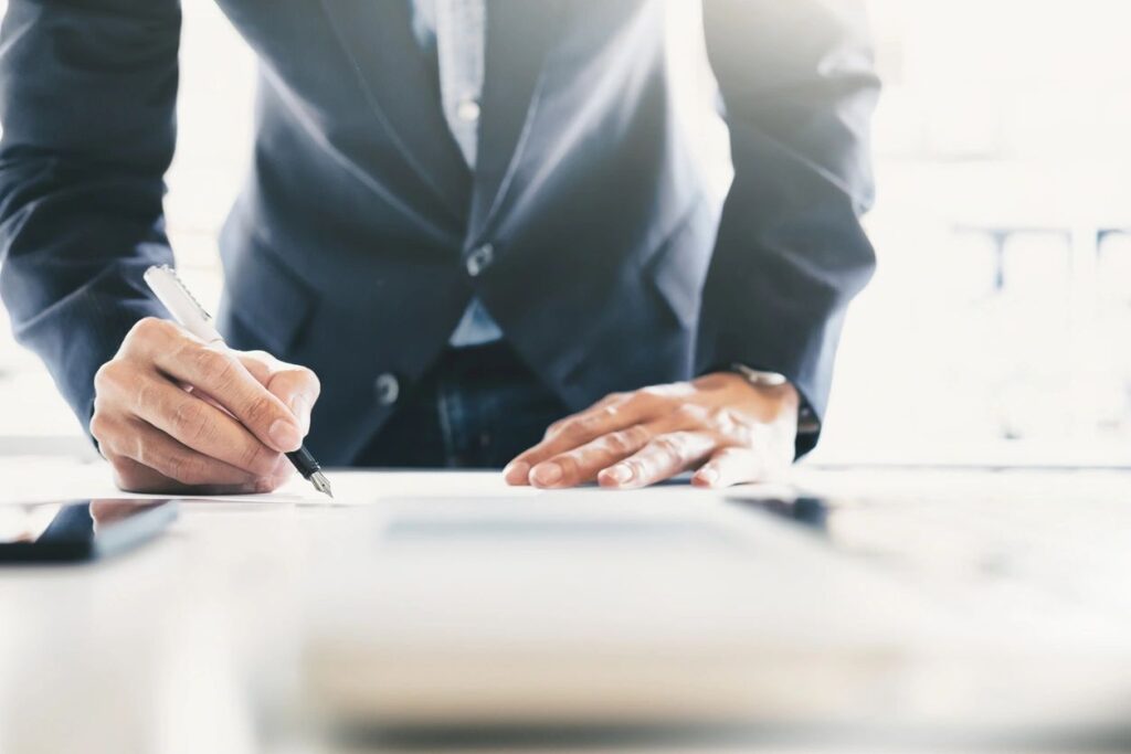 A person in a suit signing a document on a desk.