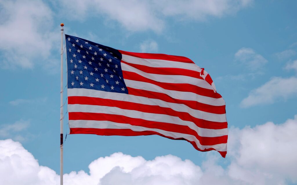 American flag waving against a blue sky with clouds.